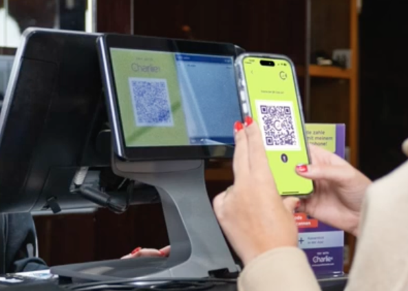 Eine Frau mit Taschen in der rechten Hand schaut fröhlich auf ihr Smartphone.