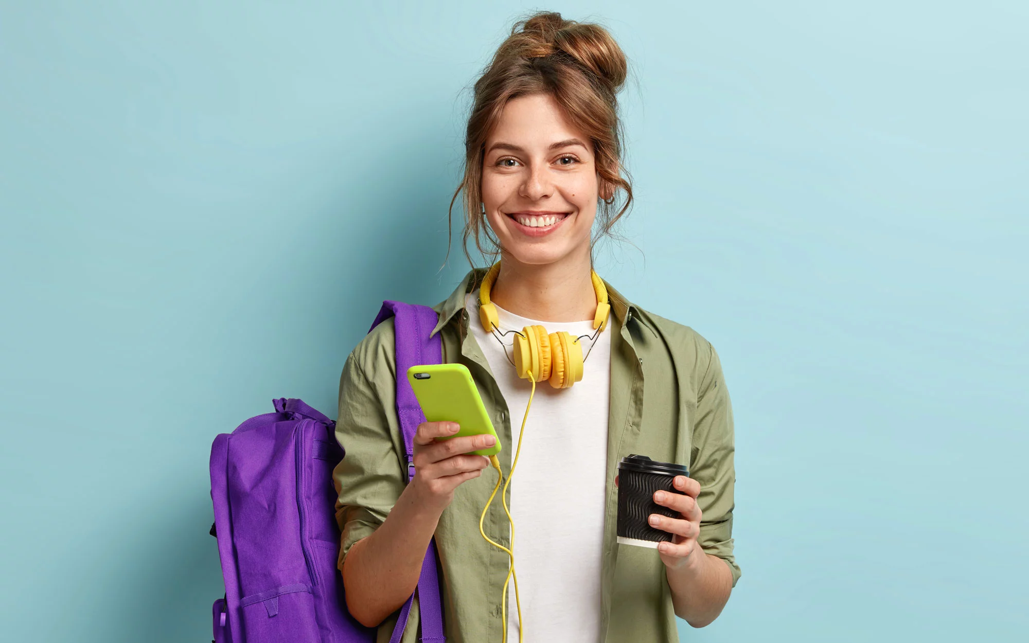 Eine lächelnde Frau hält einen Kaffeebecher und ein Smartphone in ihrer Hand.