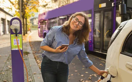 Eine lächelnde Frau tankt ihr Elektroauto an einer E-Ladesäule und bezahlt mit Pay with ME.
