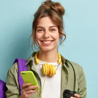 Eine lächelnde Frau hält einen Kaffeebecher und ein Smartphone in ihrer Hand.